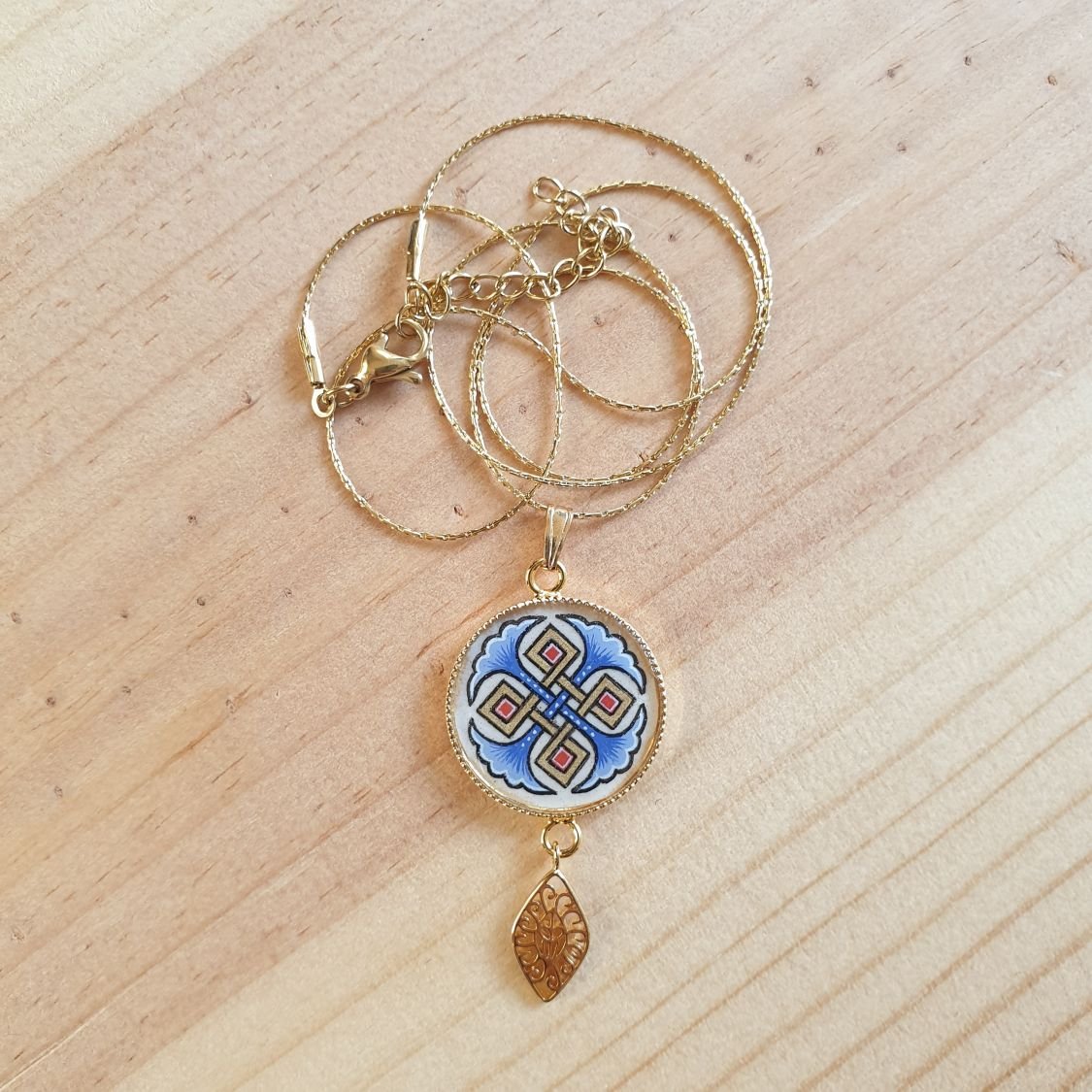 Halsbands hängen belyst med blå palmetter, guld och röda flätningar på guldkedja.