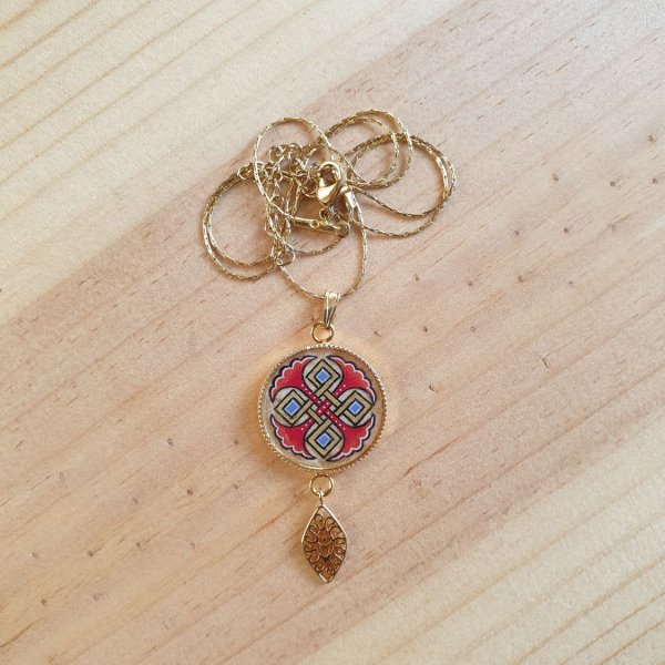 Halsbands h&auml;ngen belyst med bl&aring; palmetter, guld och r&ouml;da fl&auml;tningar p&aring; guldkedja.