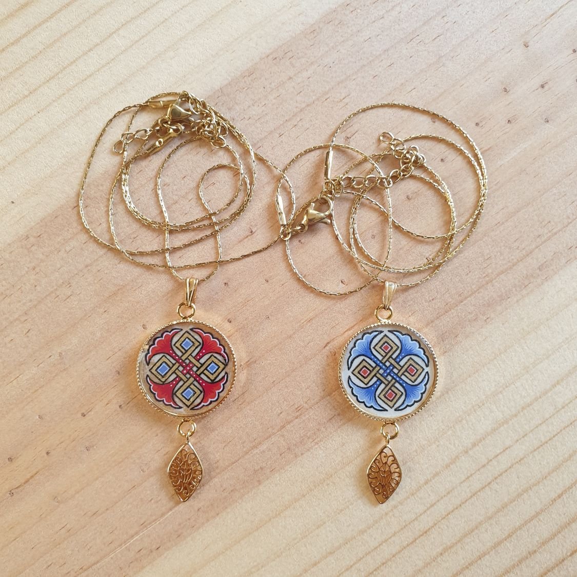 Halsbands hängen belyst med blå palmetter, guld och röda flätningar på guldkedja.