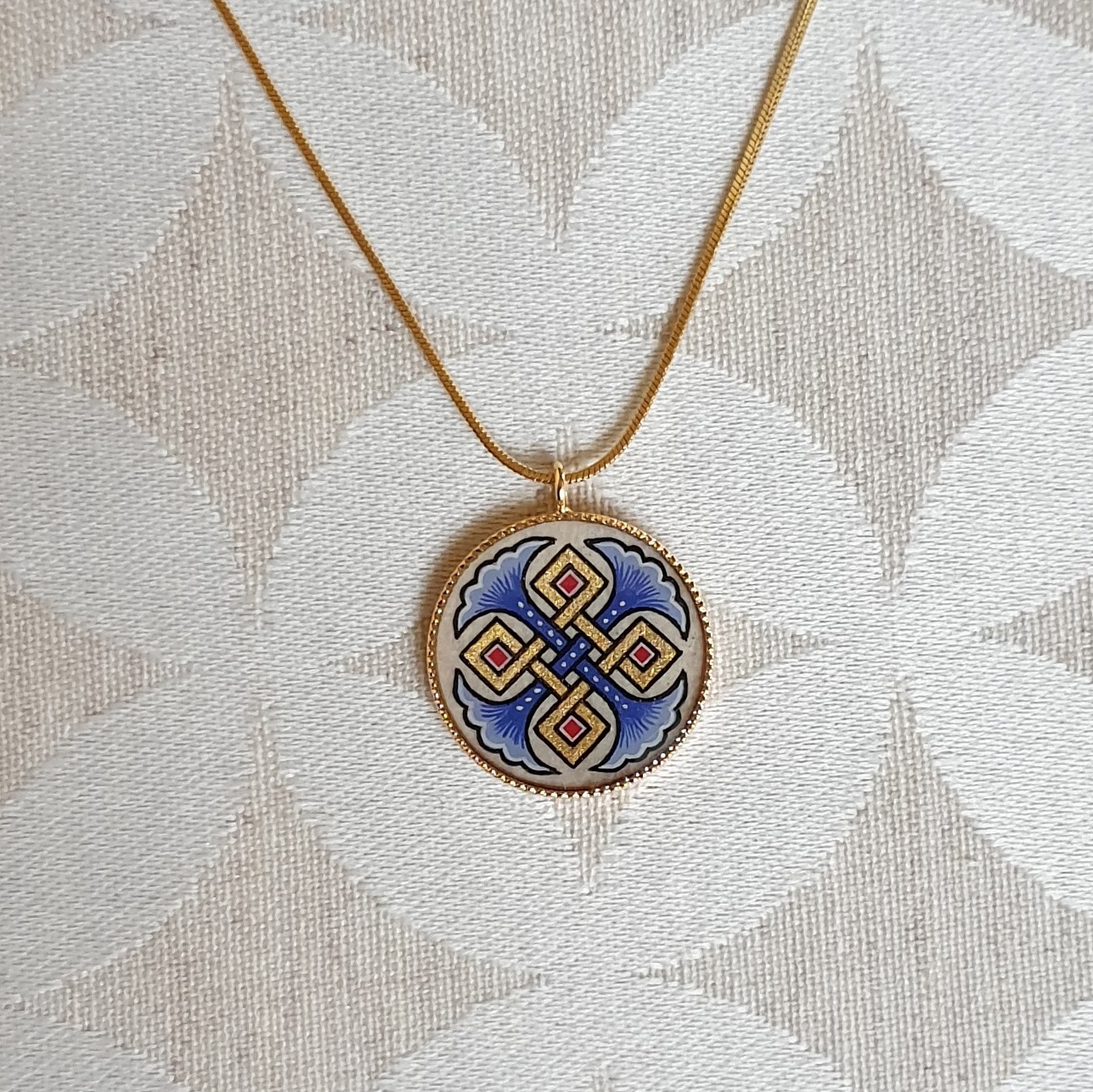 Halsband med hängande halsband med blå palmetter, guld och röda flätningar på guldkedja.