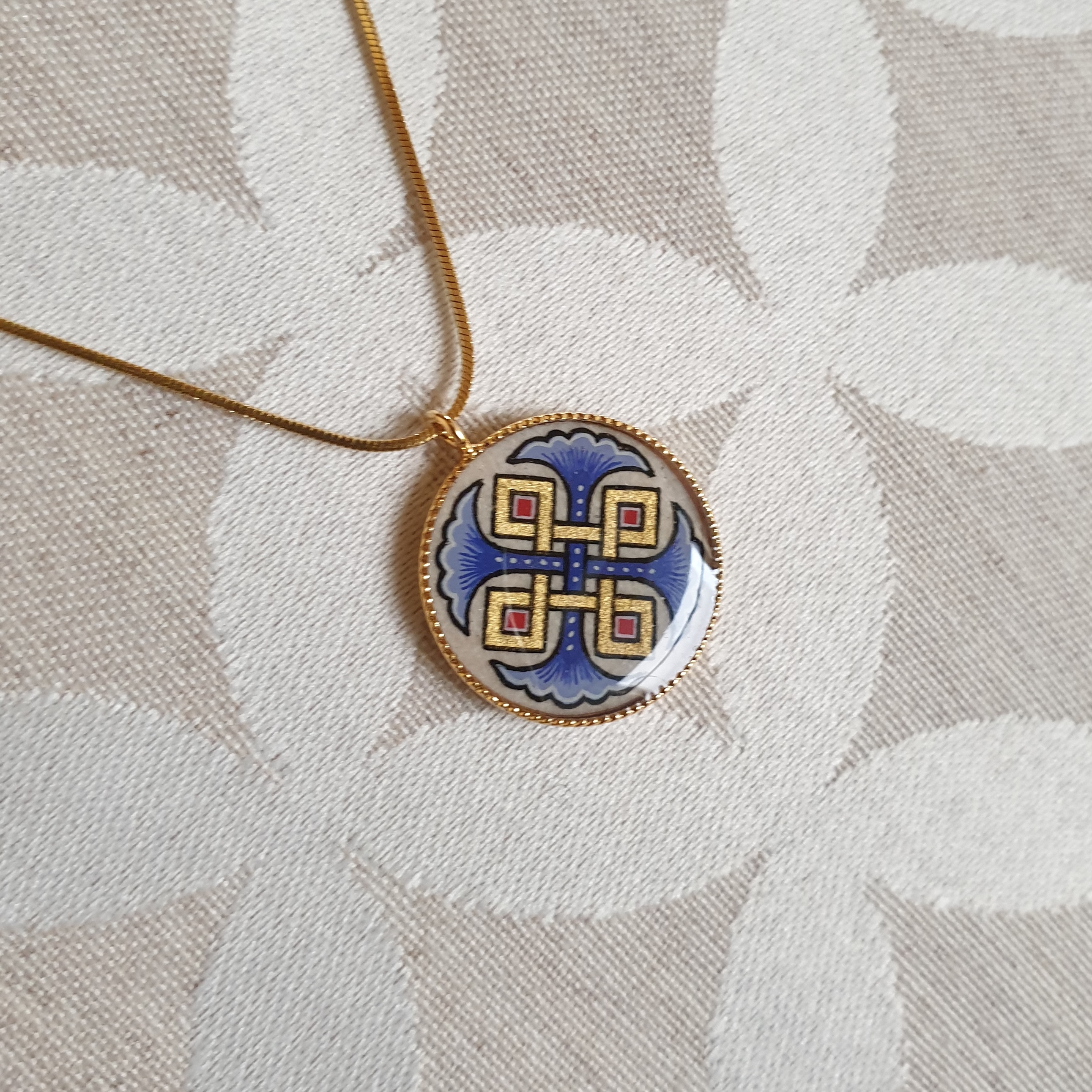 Halsband med hängande halsband med blå palmetter, guld och röda flätningar på guldkedja.
