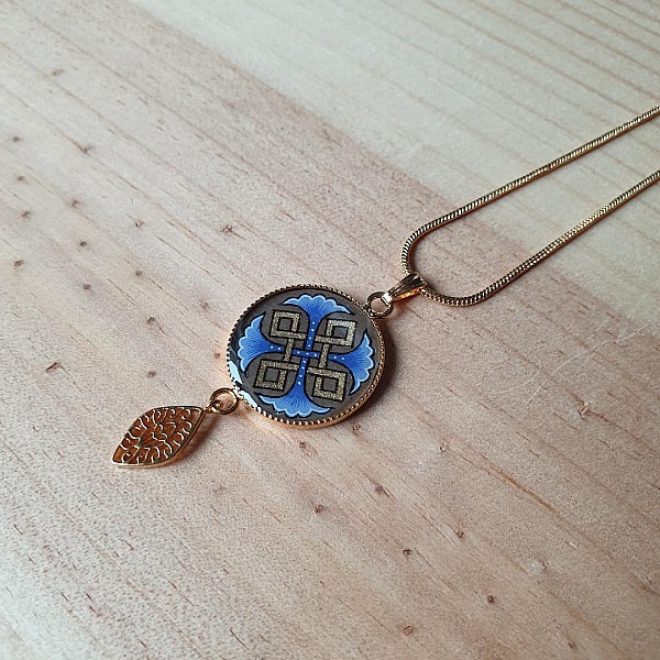 Collier pendentif doré avec médaillon bleu à motifs entrelacs.